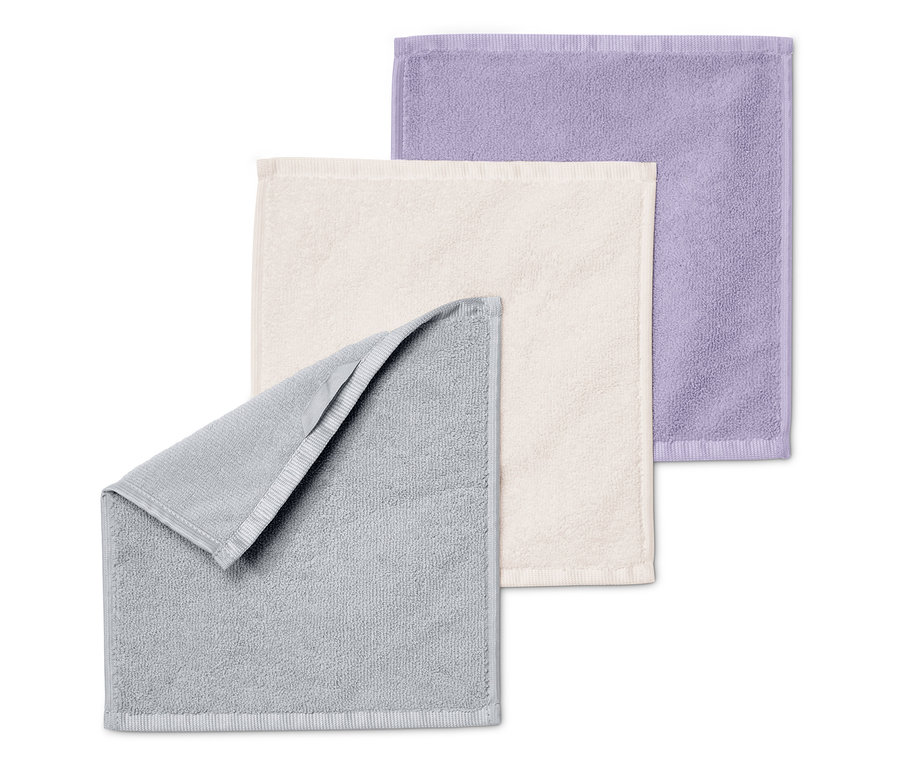 Trois serviettes pliées les unes sur les autres : grise, crème et violette.