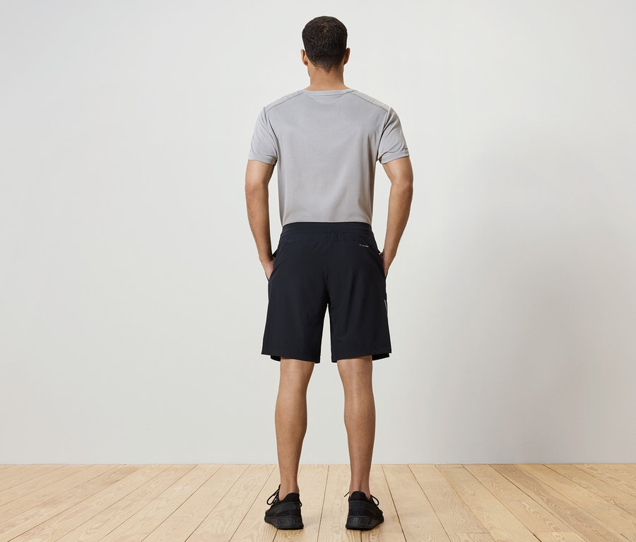 Un homme, dos à la caméra, porte un t-shirt gris, un short noir et des chaussures noires.