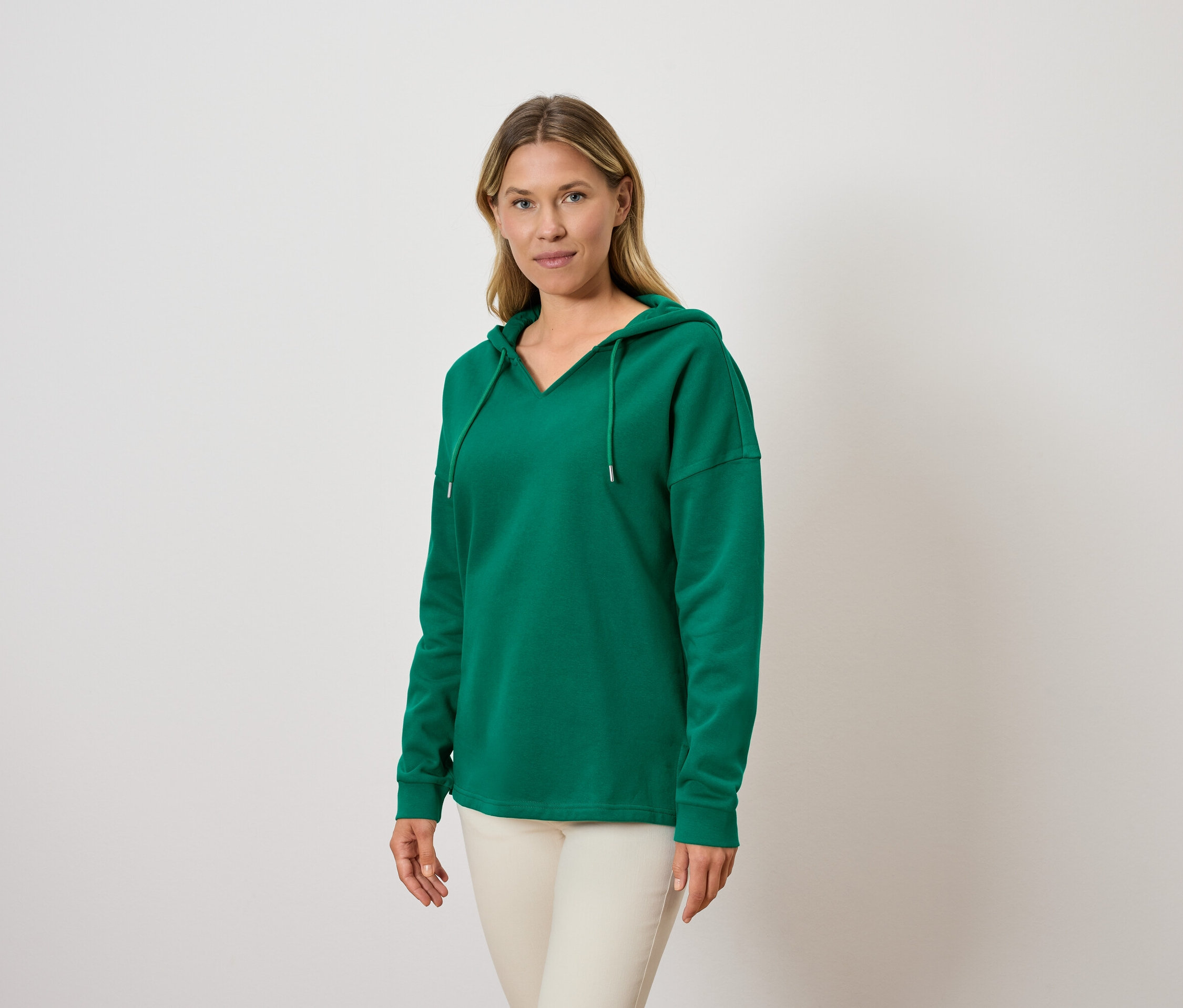 Une femme porte un sweat à capuche vert et un pantalon clair.