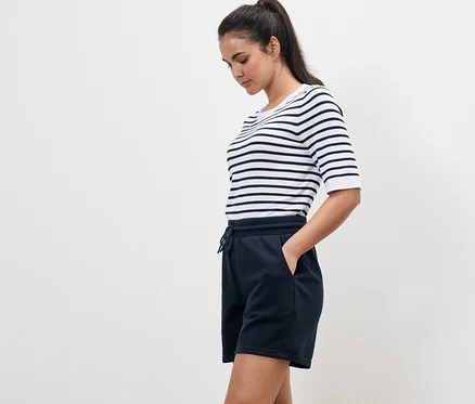 Femme portant un t-shirt rayé et un short molletonné bleu marine, debout de profil.
