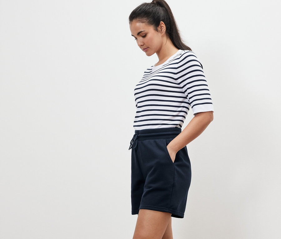 Femme portant un t-shirt rayé et un short molletonné bleu marine, debout de profil.