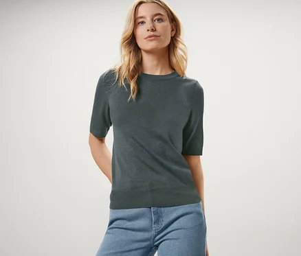 Une femme pose avec un pull en maille fine vert et un jean bleu.