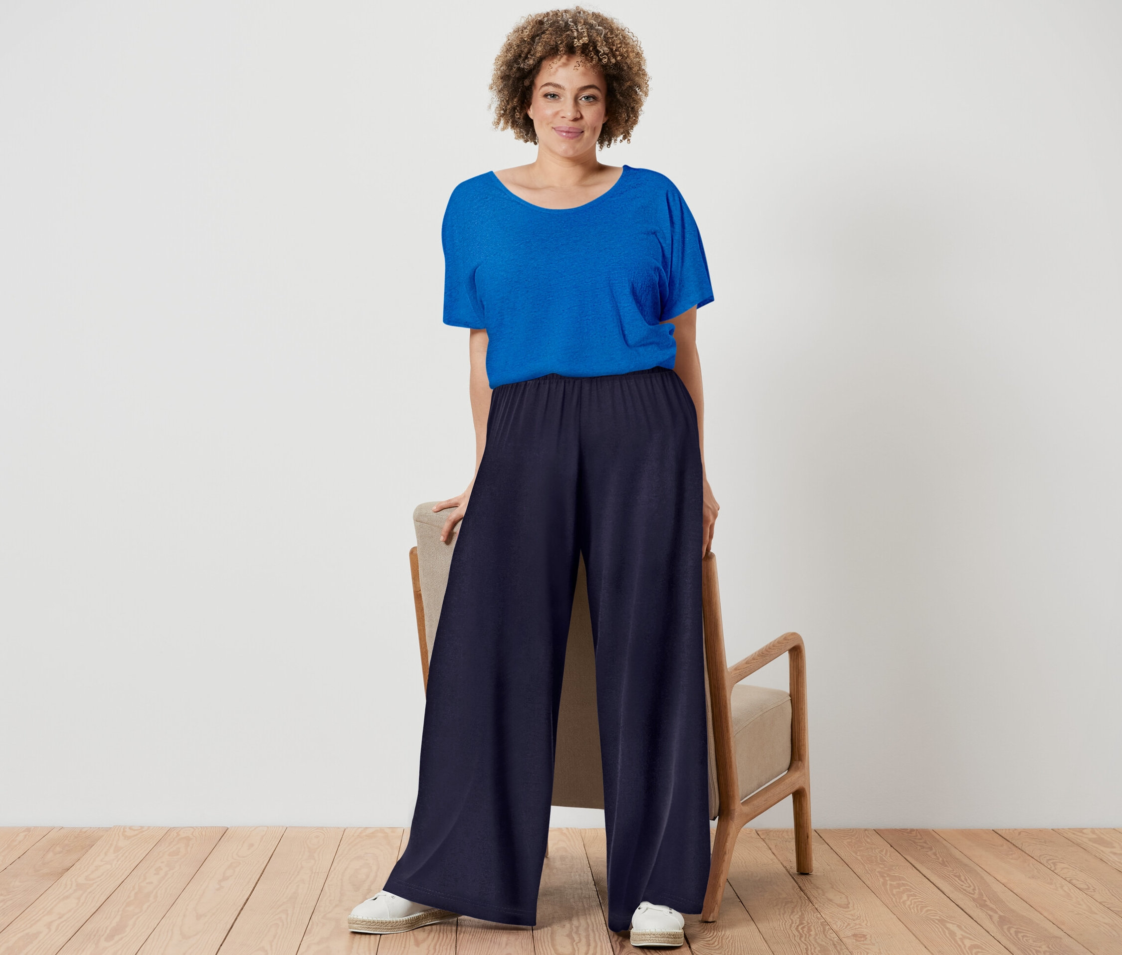 Une femme pose, portant un t-shirt en lin mélangé bleu cobalt et un pantalon palazzo bleu foncé.