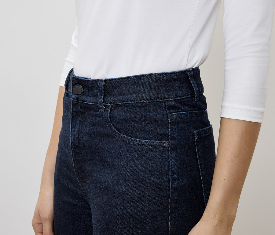 Une femme porte un jean bleu foncé et un t-shirt blanc à manches longues.