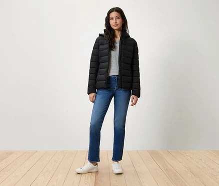 Une femme debout portant une doudoune noire, un jean bleu et des baskets blanches.