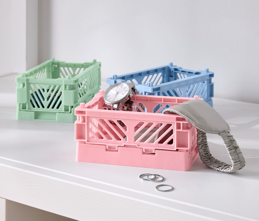 Trois boîtes pliantes colorées sur une table, une rose avec une montre, une bleue et une verte.