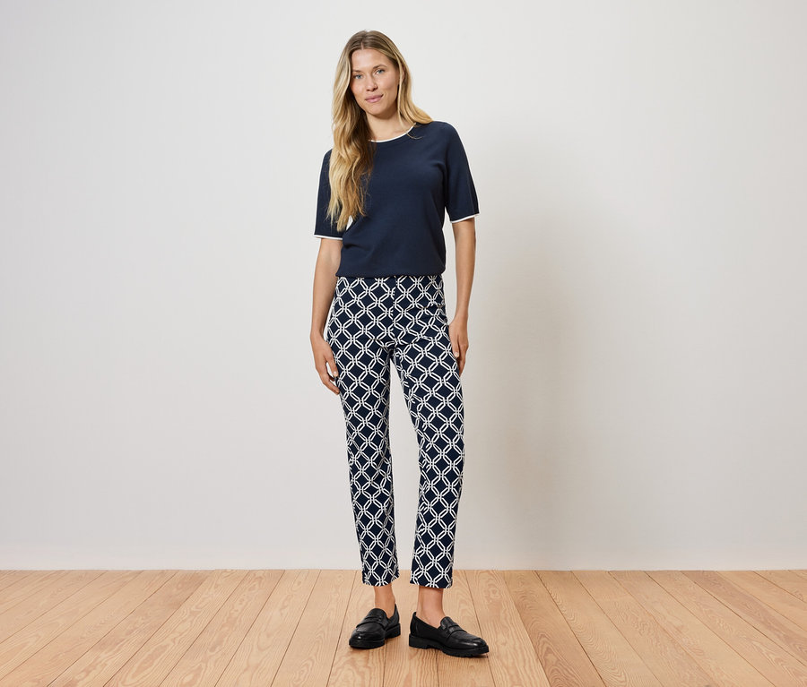 Une femme se tient sur un plancher en bois, portant un t-shirt bleu marine et un pantalon à motifs.