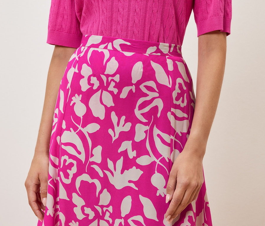 Une femme porte un haut rose et une jupe à fleurs.