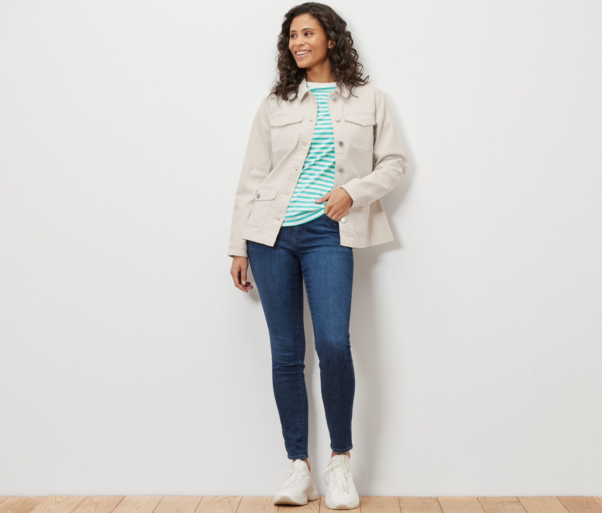 Une femme porte une veste en jean avec des poches cargo, un jean bleu et des baskets blanches.