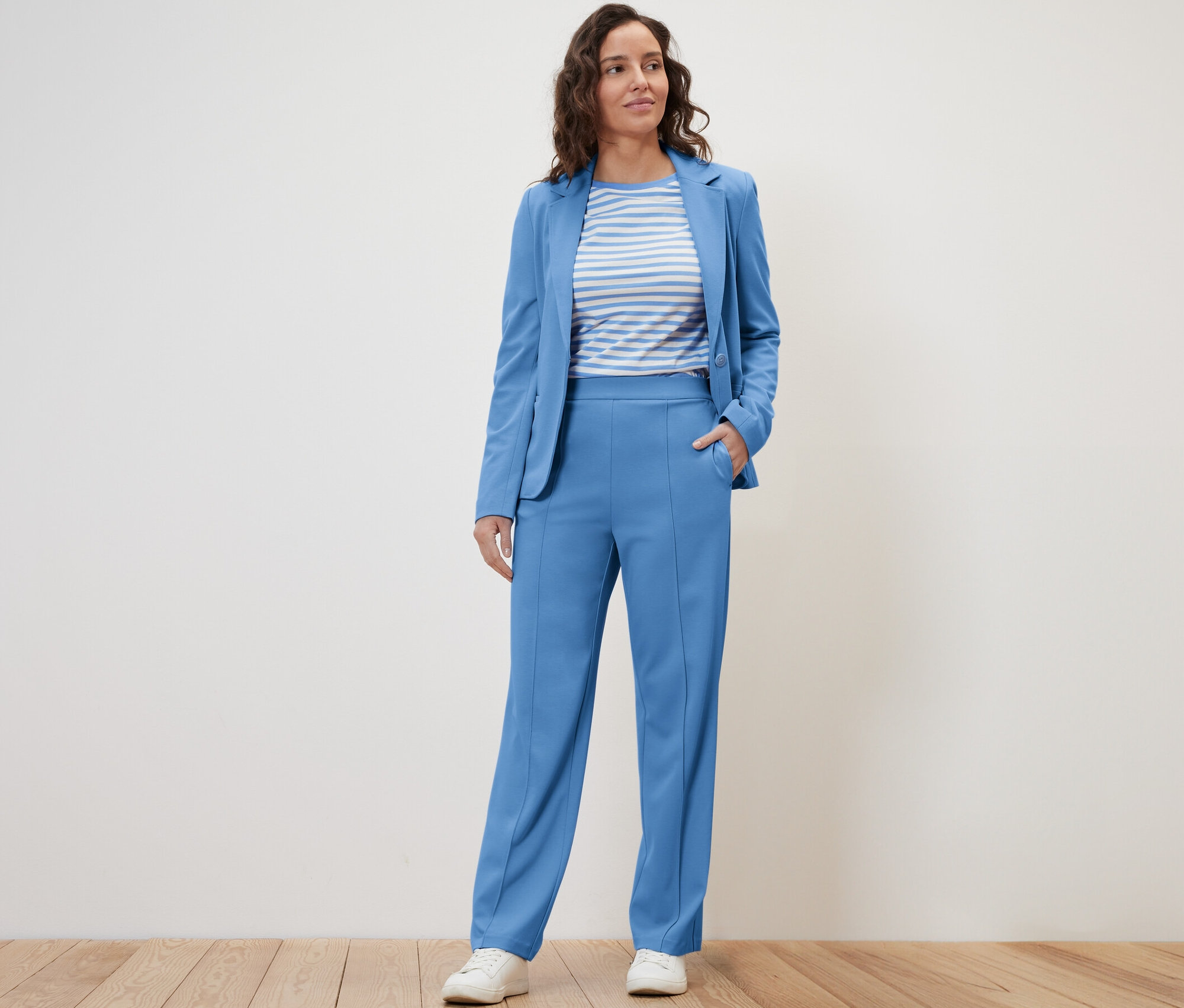Une femme pose en veste bleue et pantalon en jersey avec passepoil.