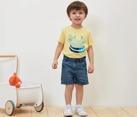 Garçon debout à côté d'un short en jean pour enfant et d'un jouet dans un trotteur.