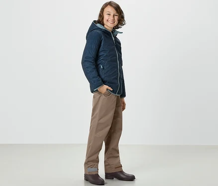 Un garçon en veste et Kinder-Regenhose se tient de côté.