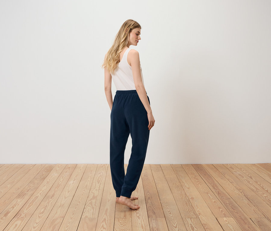 Une femme, dos à la caméra, porte un débardeur blanc et un pantalon de survêtement bleu marine.