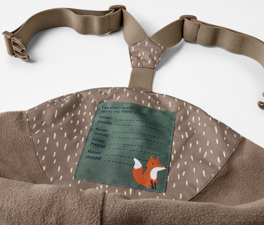 Détail du pantalon de pluie thermique pour enfant avec bretelles et imprimé ours, avec étiquette de nom et illustration de renard.