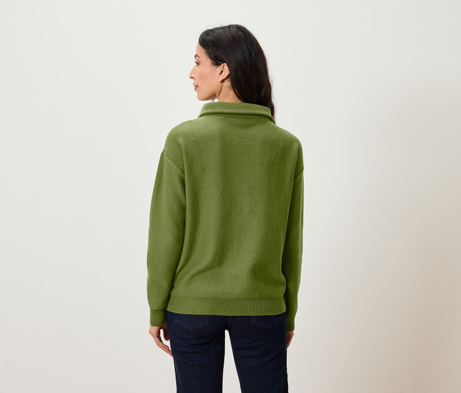 Une femme, vue de dos, porte un pull vert et un jean.