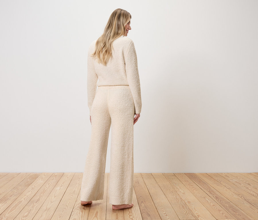 Femme debout de dos, vêtue d'un pull et d'un pantalon large en tricot bouclé.