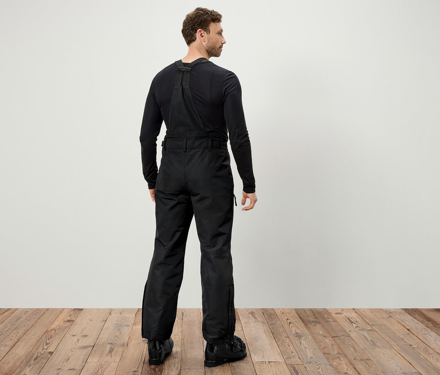 Un homme, vu de dos, porte un pantalon de ski noir à bretelles et des chaussures de ski noires.