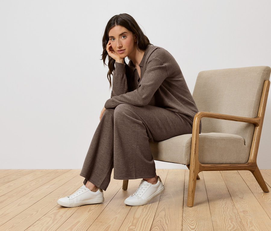 Une femme est assise dans un fauteuil, portant des vêtements marron et des chaussures blanches.