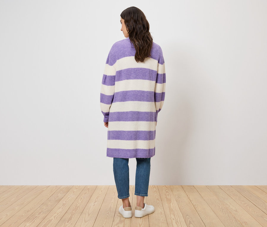 Vue arrière d'une femme portant un manteau rayé violet et blanc, un jean et des chaussures blanches.
