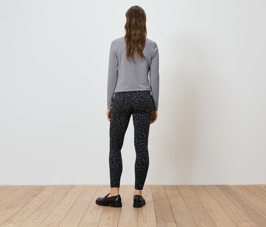 Une femme, vue de dos, porte un t-shirt gris à manches longues et un legging noir.