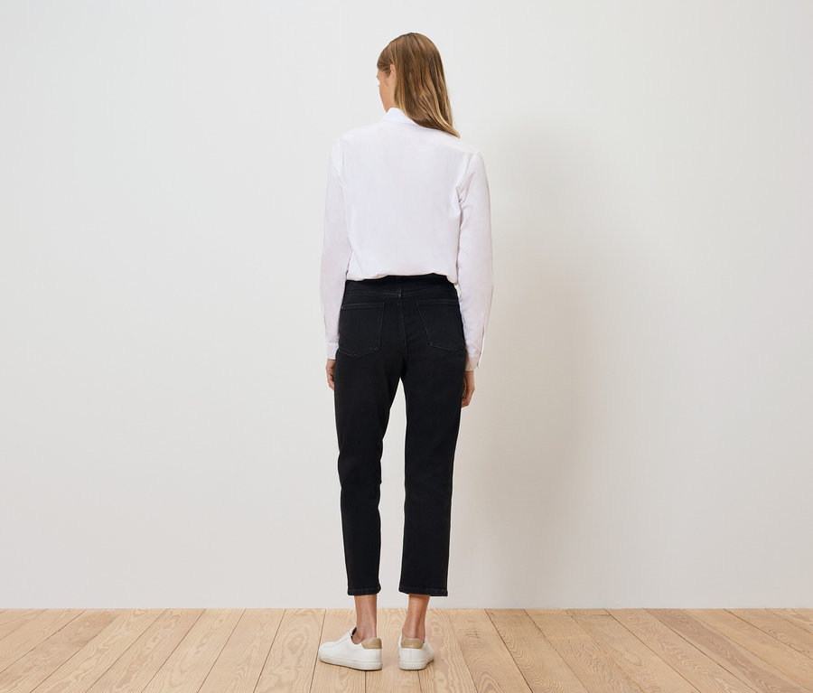 Vue de dos, une femme porte une chemise blanche, un pantalon noir et des chaussures blanches.