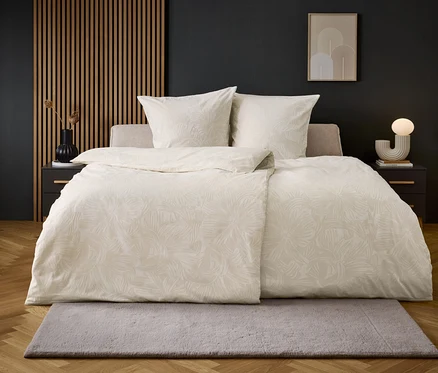 Lit beige avec des draps blancs sur un sol avec un tapis gris.