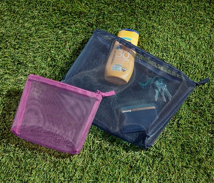 Deux pochettes de rangement sont posées sur l'herbe. L'une contient de la crème solaire, des clés et une carte.