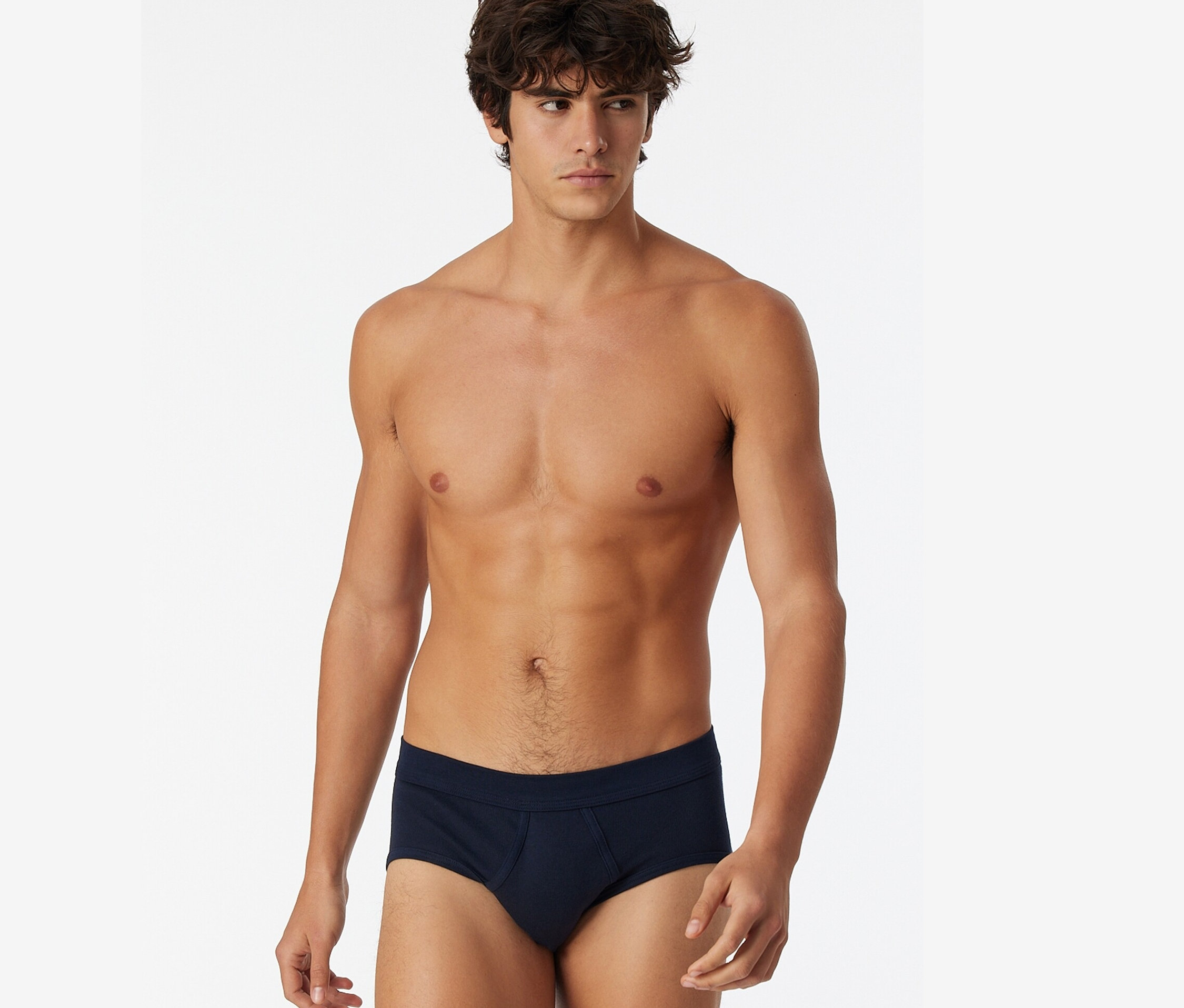 Un homme pose torse nu et porte 2 slips de sport SCHIESSER bleu marine.