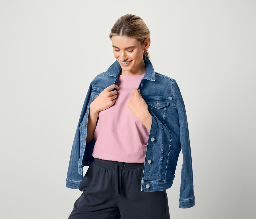 Une femme portant une veste en jean, un t-shirt basique rose et un sweatshort bermuda.
