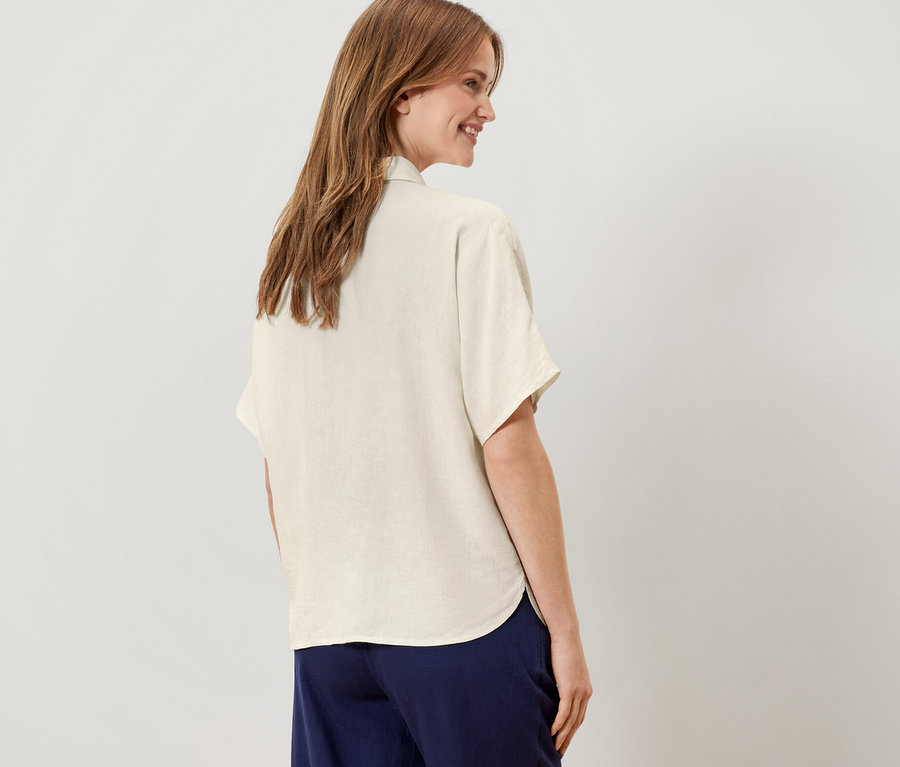Une femme, vue de dos, porte un chemisier en lin blanc crème.