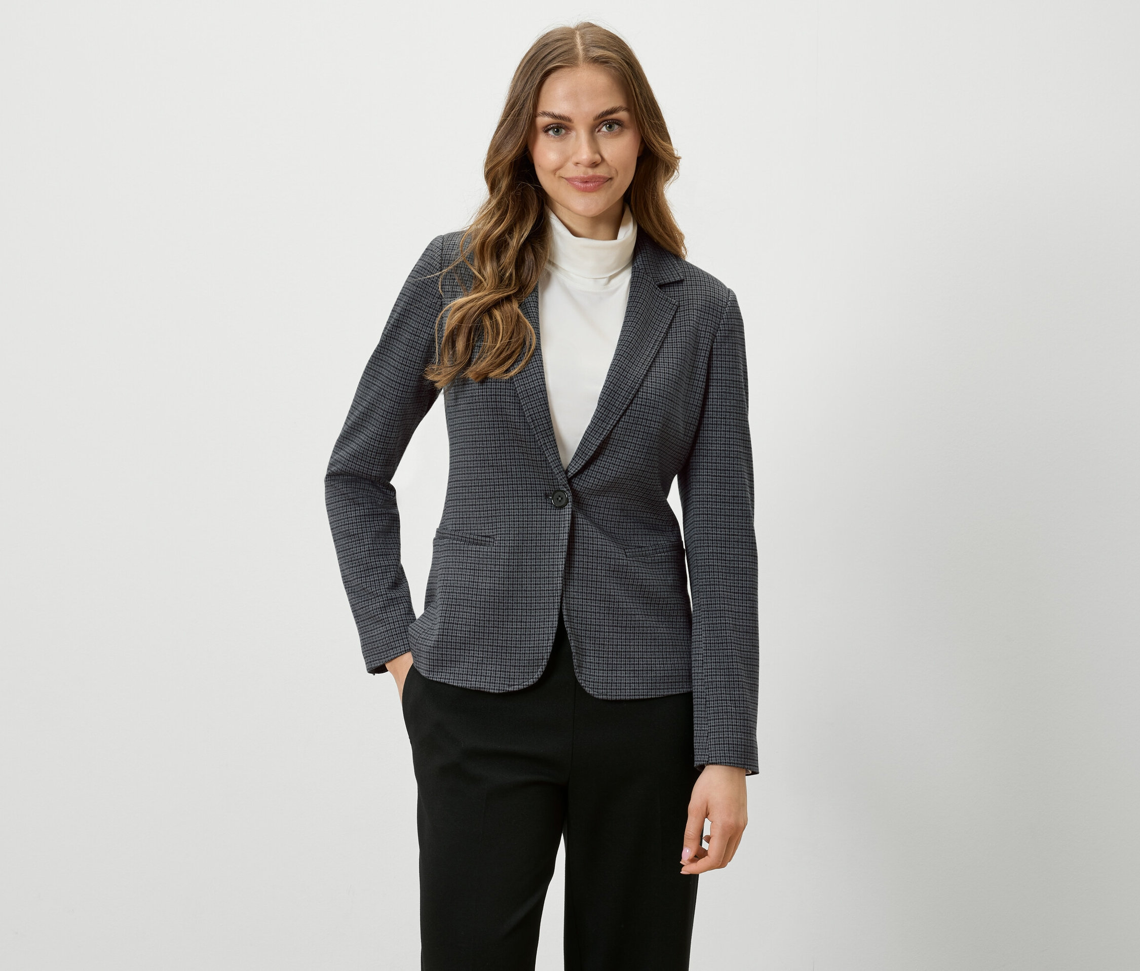 Une femme aux cheveux bruns porte un blazer à carreaux et un pantalon noir.