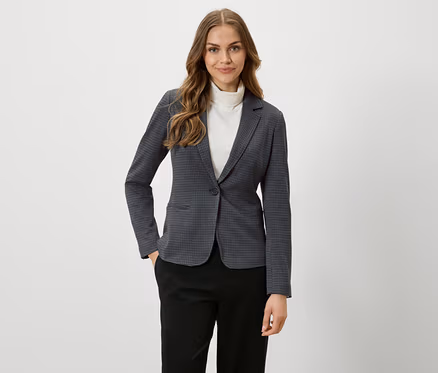 Une femme aux cheveux bruns porte un blazer à carreaux et un pantalon noir.