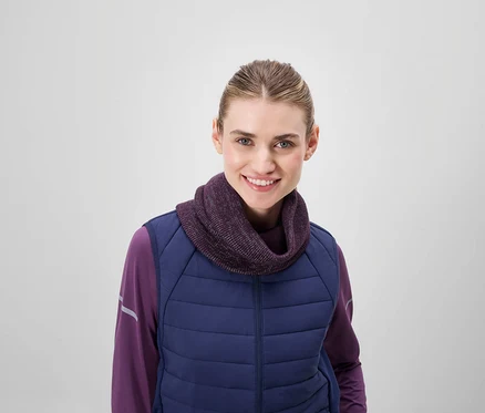 Une femme souriante porte un col roulé violet et une veste matelassée bleue.