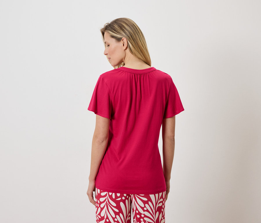 Vue arrière d'une femme blonde portant un t-shirt rose et un pantalon à motifs rouge et blanc.