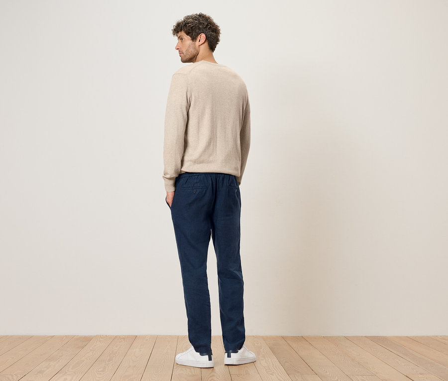Homme de dos portant un pull beige, un pantalon bleu et des baskets blanches.