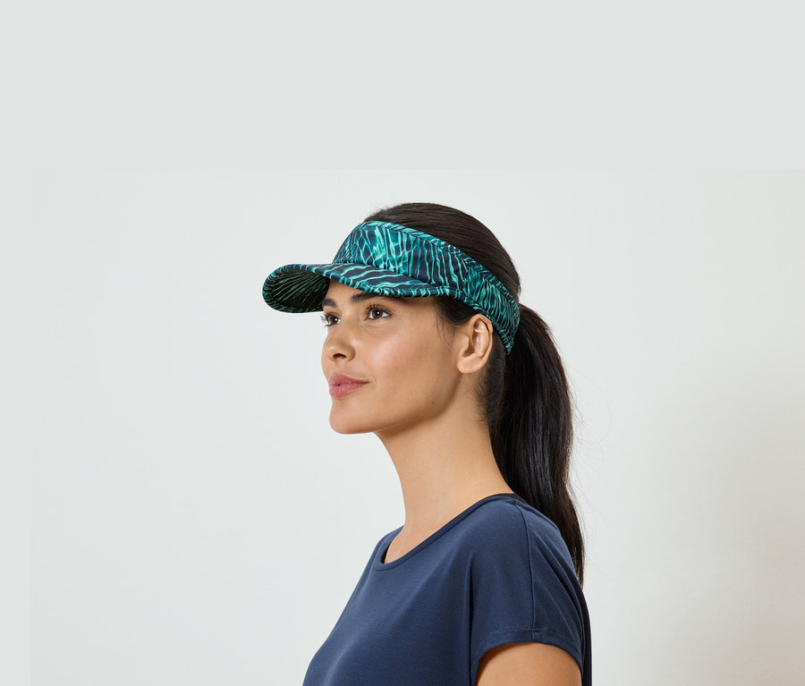 Une femme avec une queue de cheval et un t-shirt bleu porte une visière verte à motifs de feuilles.