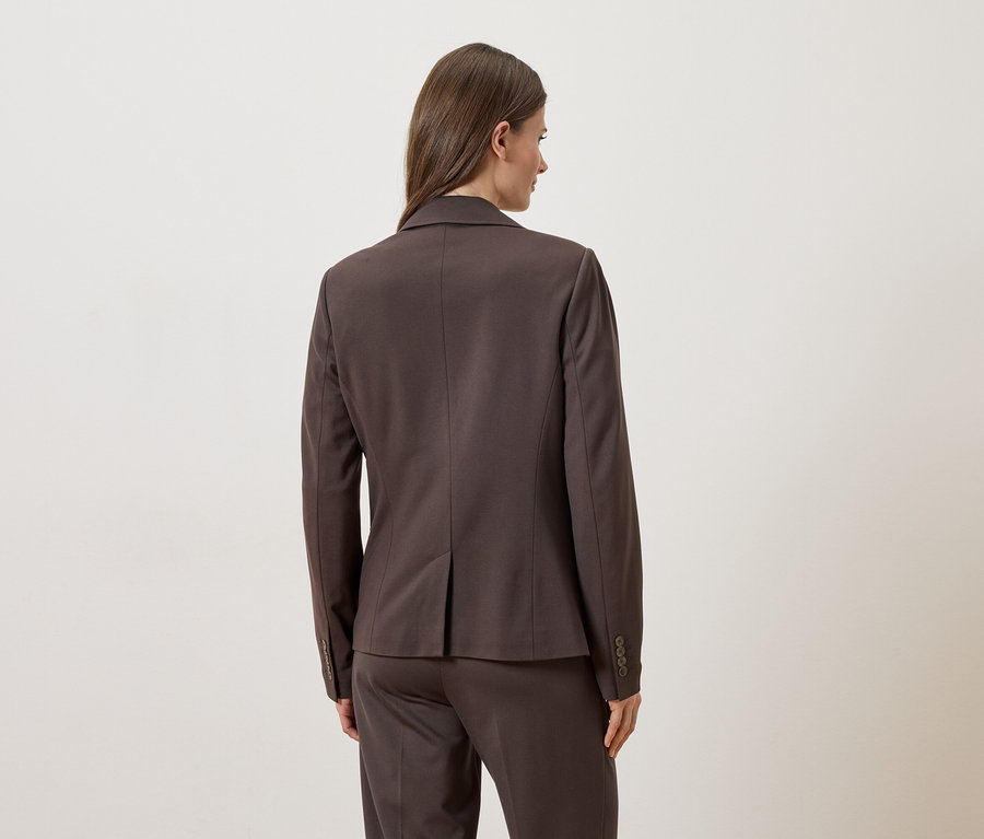 Vue arrière d'une femme portant un blazer et un pantalon marron sur fond blanc.