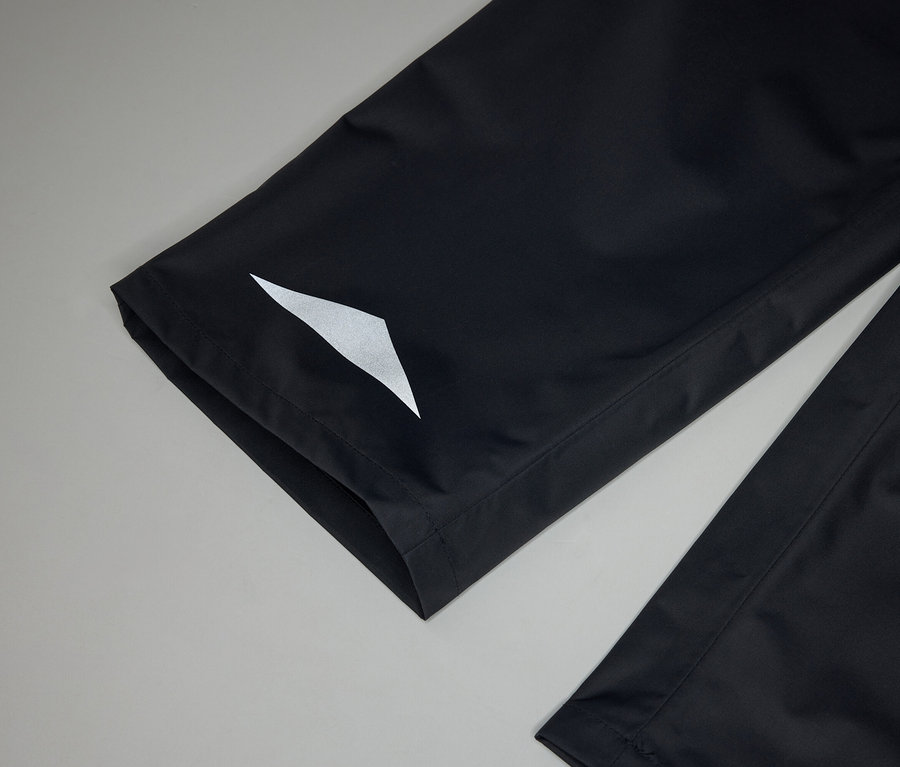 Gros plan sur des jambes de pantalon noires avec un réflecteur triangulaire blanc sur fond gris.