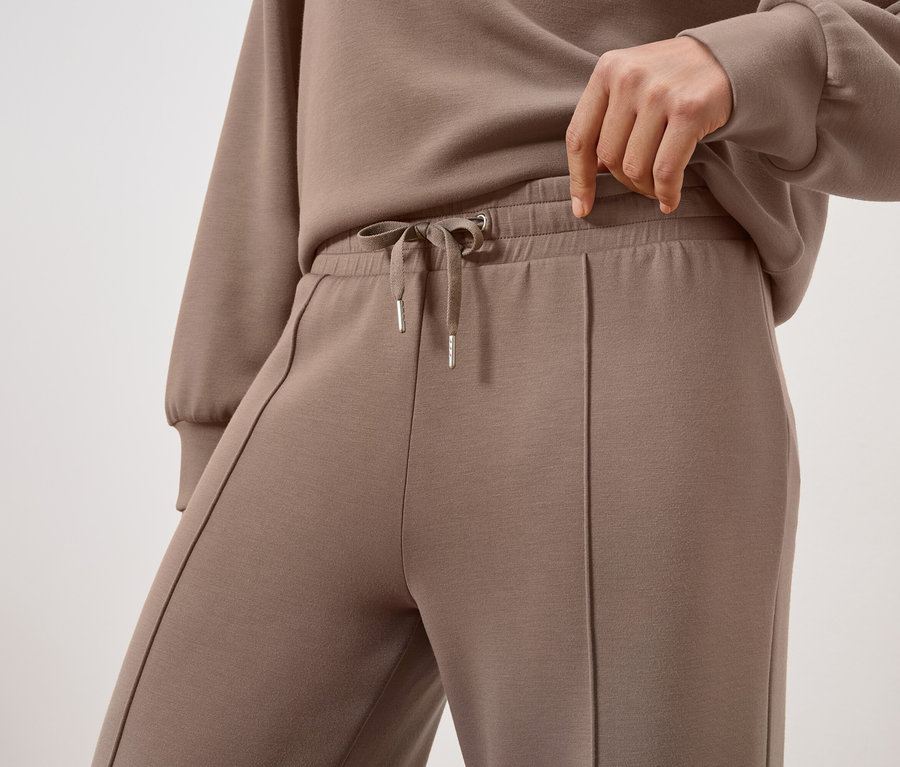 Gros plan d'une personne portant un pantalon de survêtement marron et un sweat-shirt assorti. La personne ajuste le cordon de serrage du pantalon.