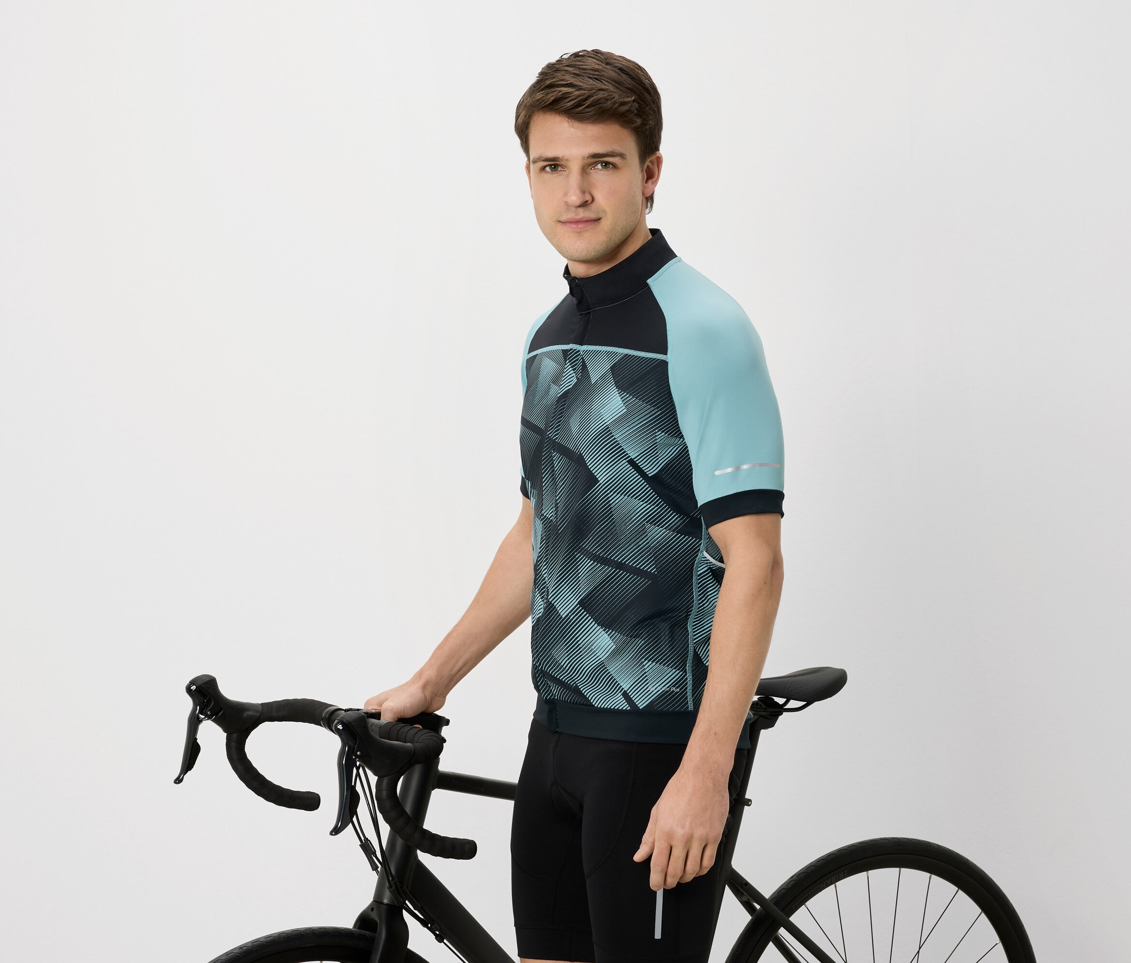 Homme en maillot de cyclisme avec des manches bleu-vert tenant un vélo noir.