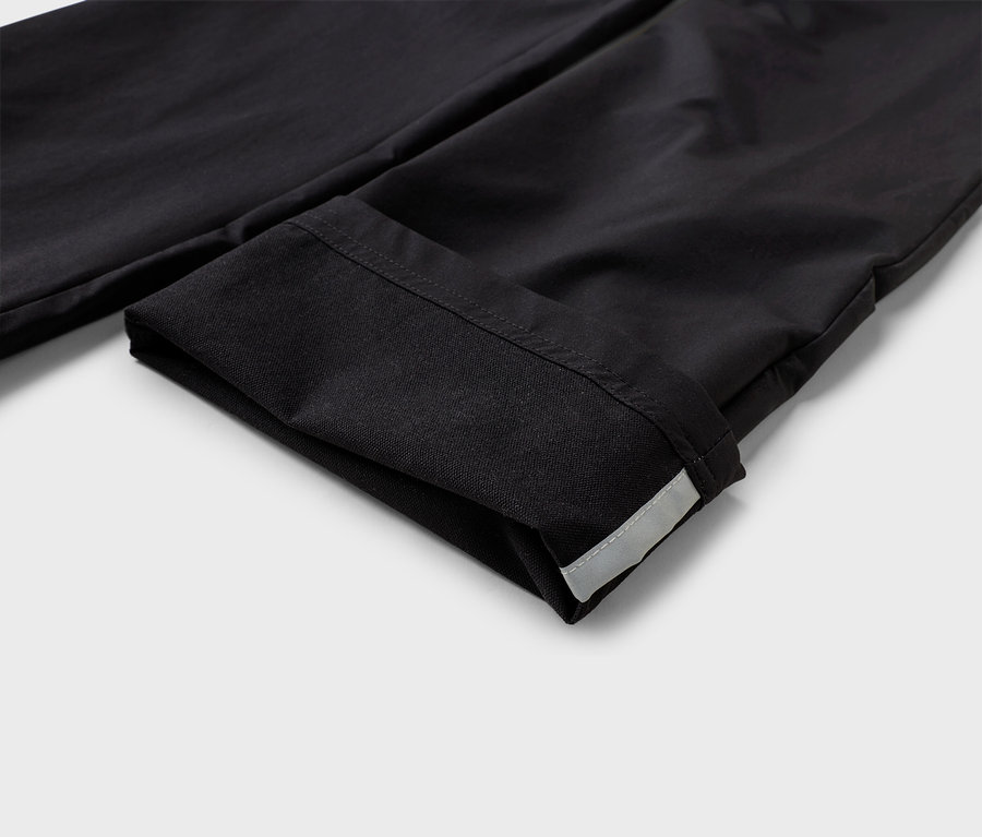Gros plan sur un pantalon en tissu noir retroussé avec une bande réfléchissante sur l'ourlet.