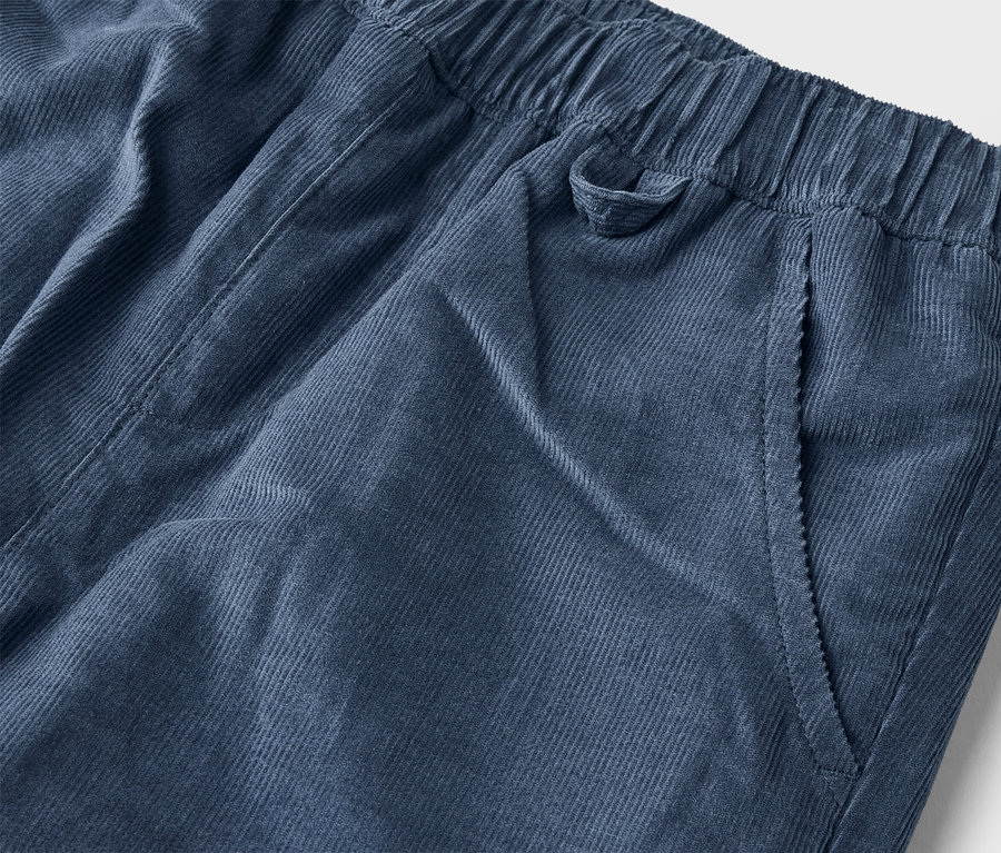 Gros plan d'un pantalon en velours côtelé bleu marine avec une taille élastiquée et une poche latérale.