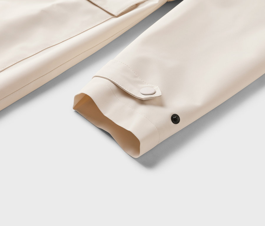 Gros plan sur la manche beige d'une veste avec des détails de boutons et une poche en arrière-plan.