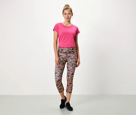 Femme debout sur fond blanc portant un t-shirt rose et un legging à fleurs.
