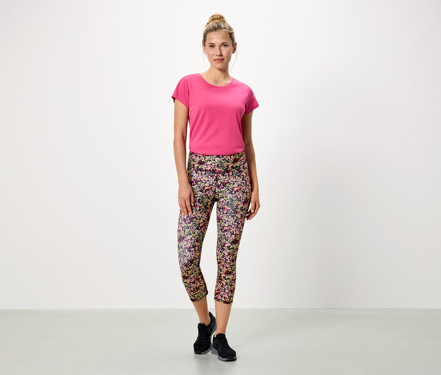 Femme debout sur fond blanc portant un t-shirt rose et un legging à fleurs.