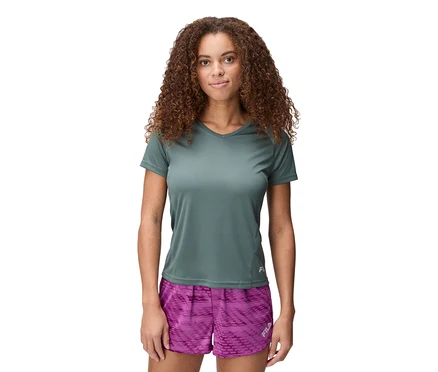 Femme aux cheveux bouclés portant un T-shirt technique pour femme FILA vert et un short violet à motifs.