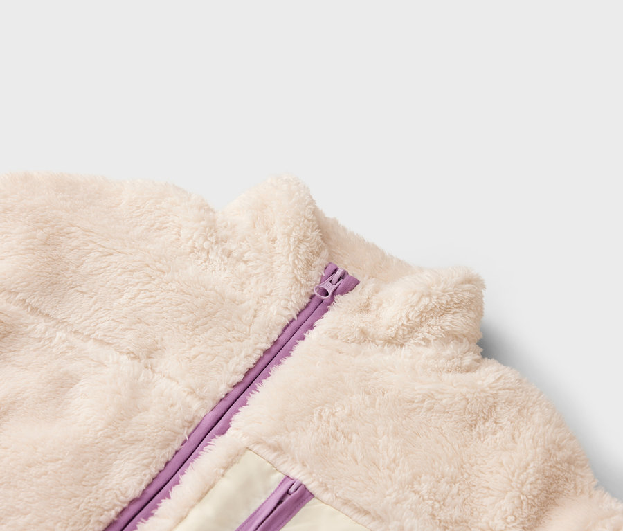 Gros plan d'une veste en polaire couleur crème avec une fermeture éclair violette.