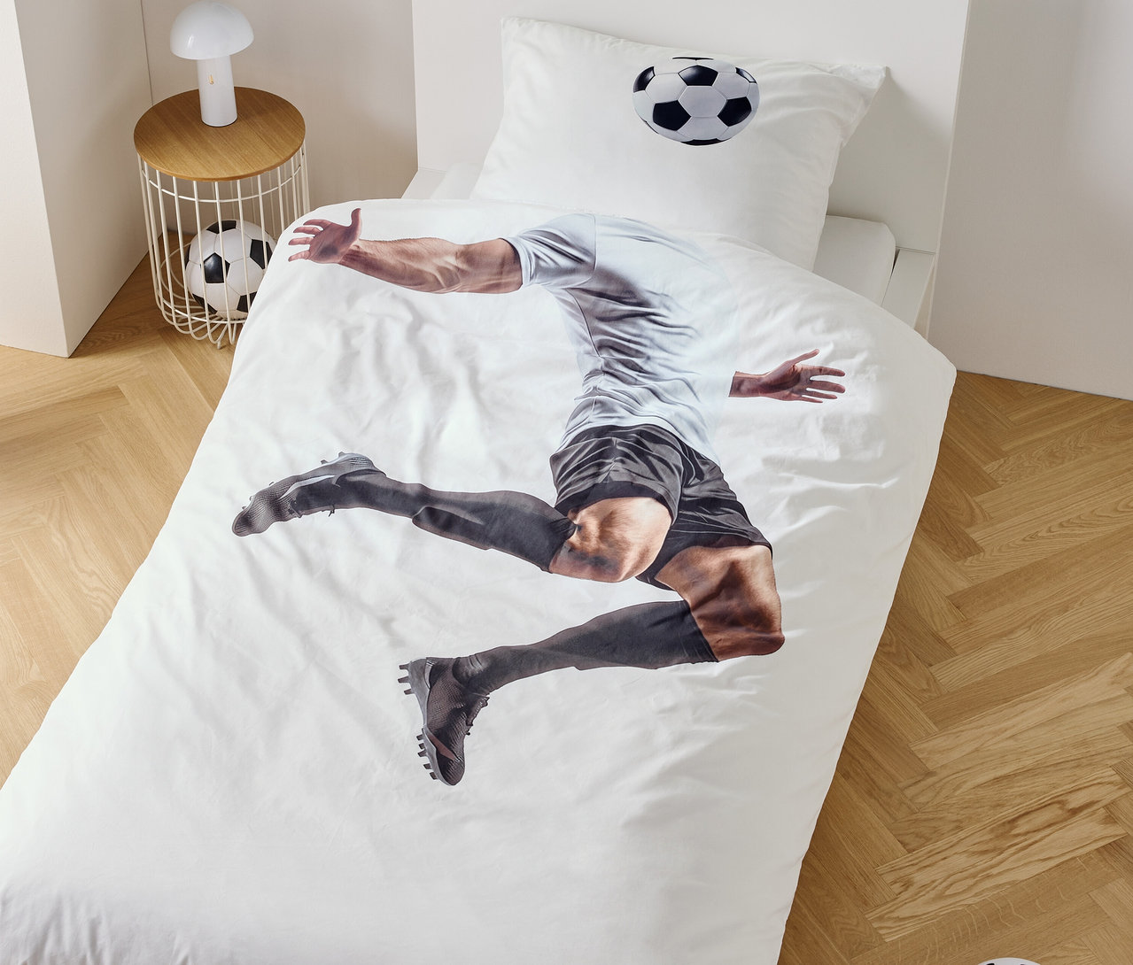Sur une housse de couette, un joueur de football est représenté en train de sauter, à côté d'une table de chevet avec une lampe et un ballon de football.