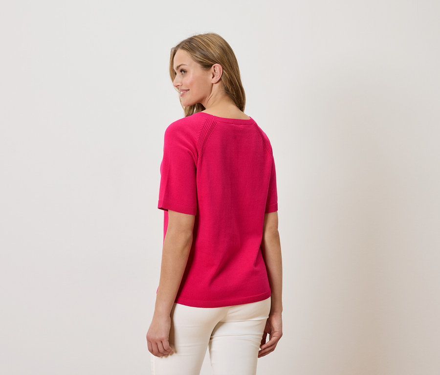 Femme portant un t-shirt rose et un pantalon blanc, vue de dos.