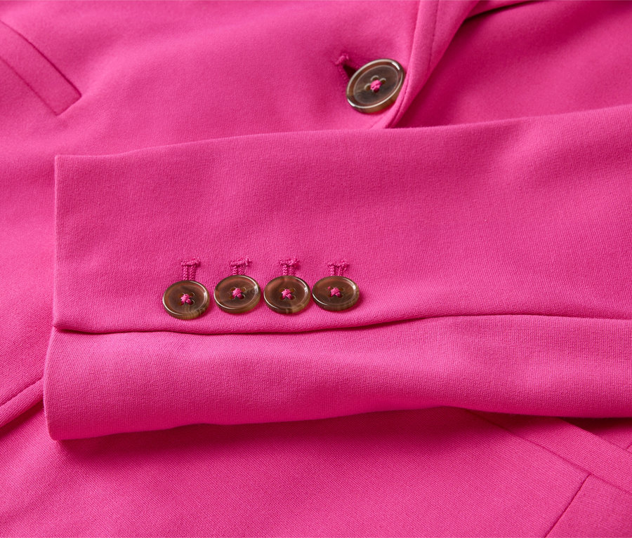Gros plan sur la manche d'un blazer rose avec quatre boutons sur la manche et un bouton sur le revers.